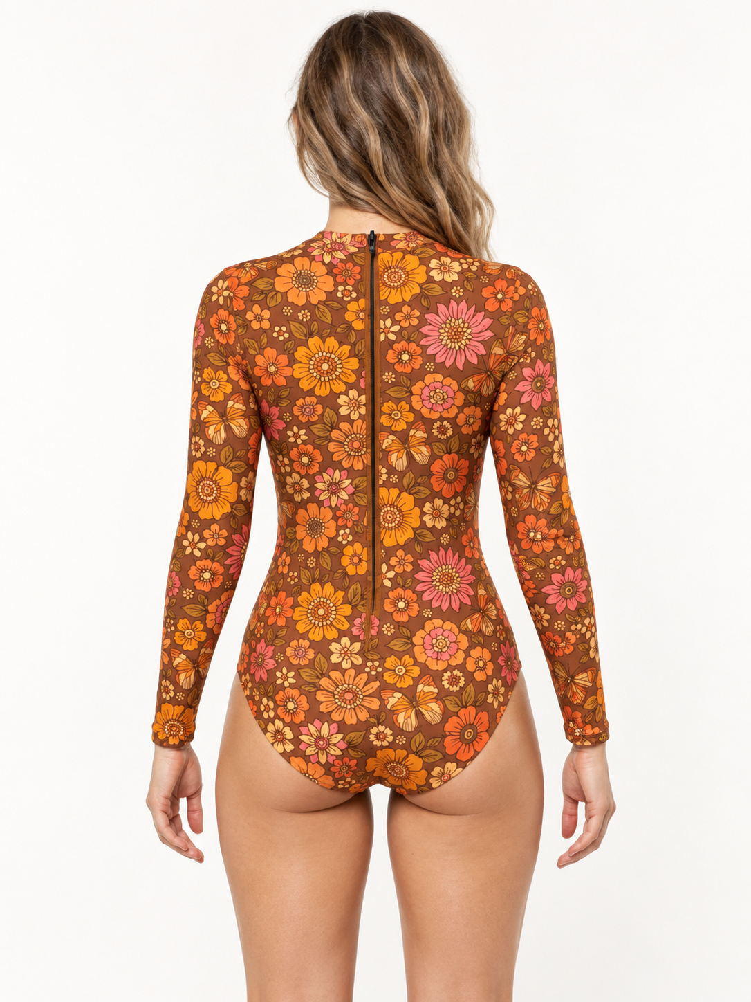 Back view of a woman in the brown Mariposa Long Sleeved Surf Suit with orange and pink flowers in a studio.