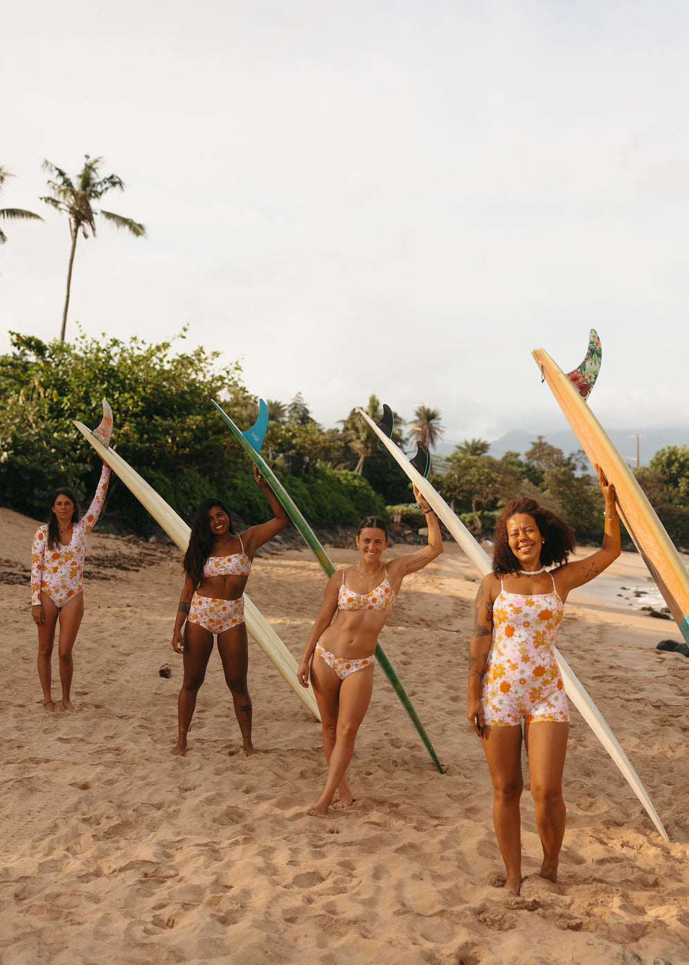 Four women in matching swimsuits holding surfboards on a beach.