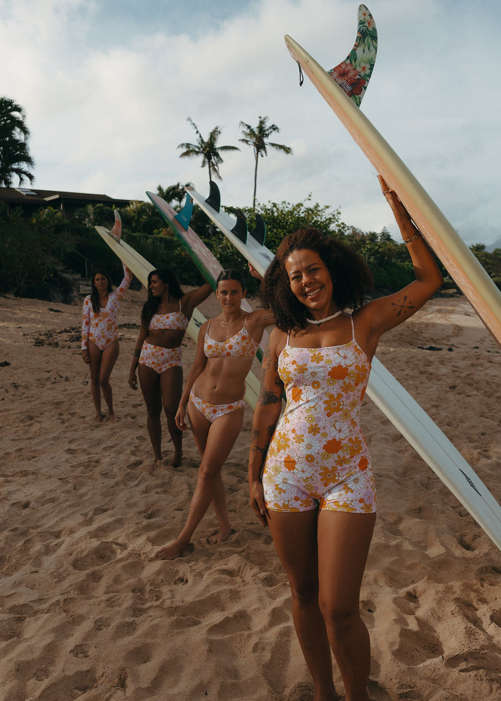 Group of women in matching sustainable swimsuits holding surfboards on a beach.